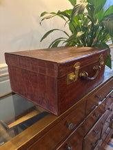 Brown crocodile skin briefcase on a reflective surface with a plant in the background