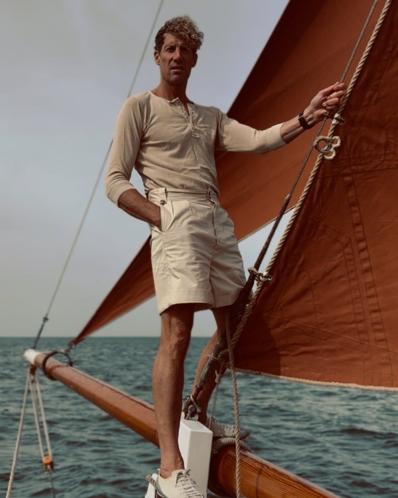 Man standing on a vintage wooden sailboat in 1920s and 30s clothing