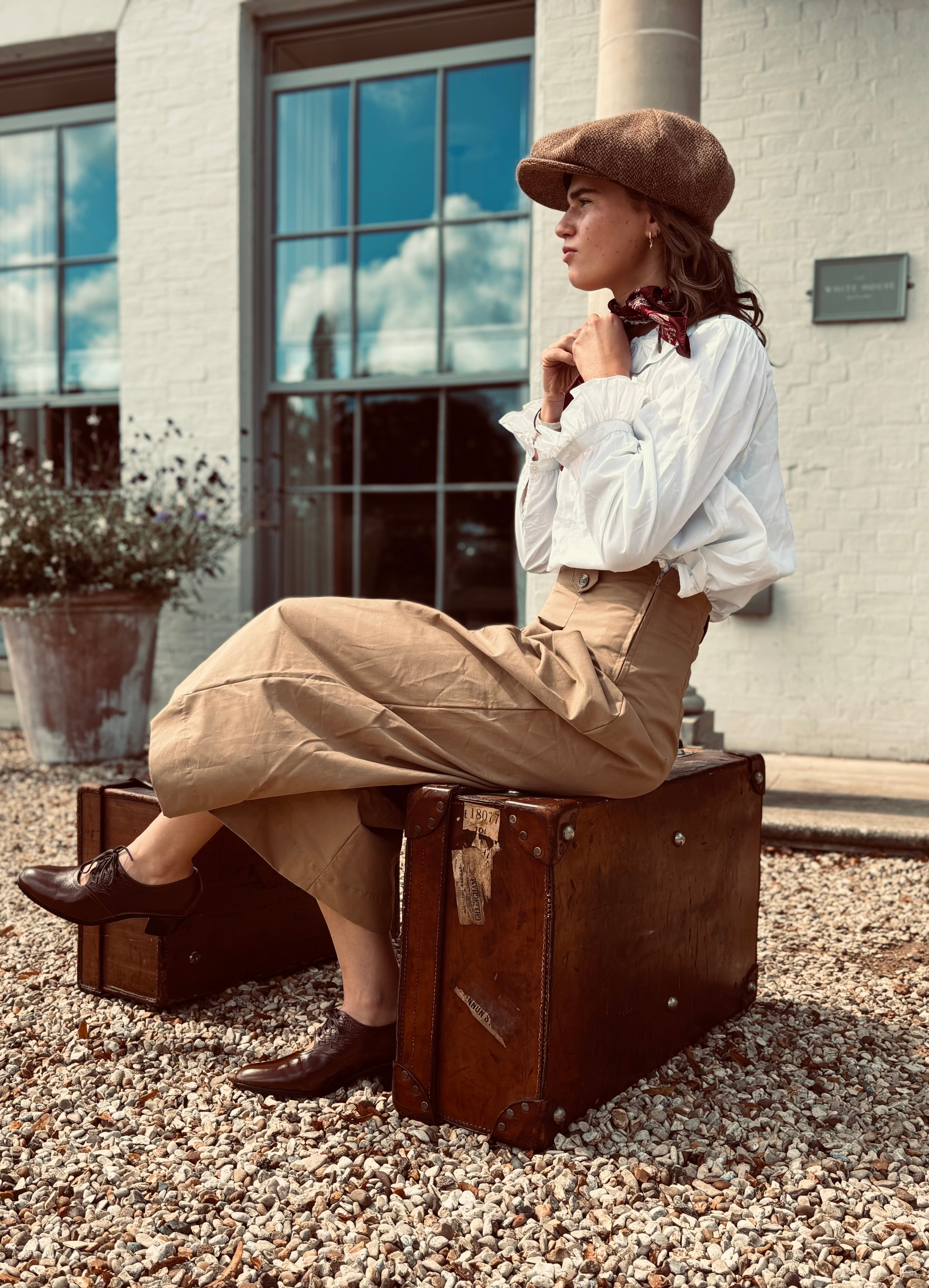 Woman in vintage attire sitting on a suitcase outdoors