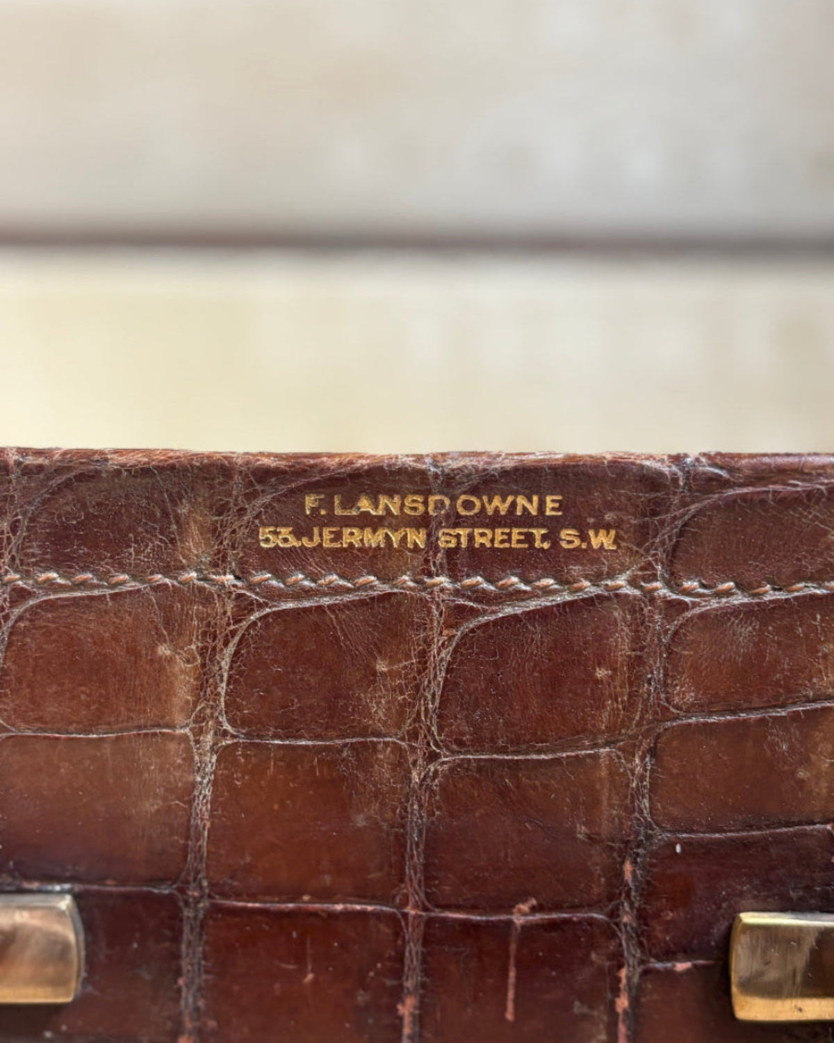 Close-up of a brown crocodile-embossed leather case with gold-toned hardware and a gold-embossed brand plaque reading 'F. LANSDOWNE 55 JERMYN STREET, S.