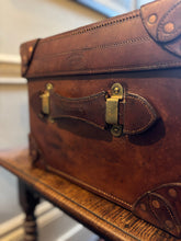 Close-up of a brown leather suitcase with brass lock on a wooden surface.