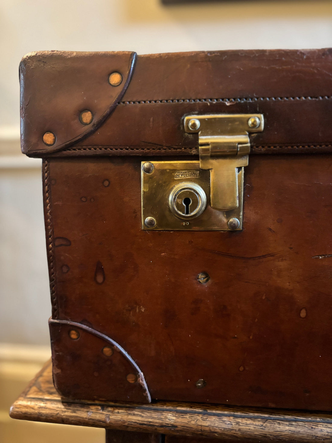 Vintage brown leather suitcase with brass lock on a wooden surface.