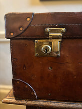 Vintage brown leather suitcase with brass lock on a wooden surface.