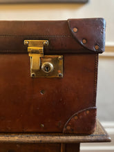 Vintage brown leather suitcase with brass lock on a wooden surface.