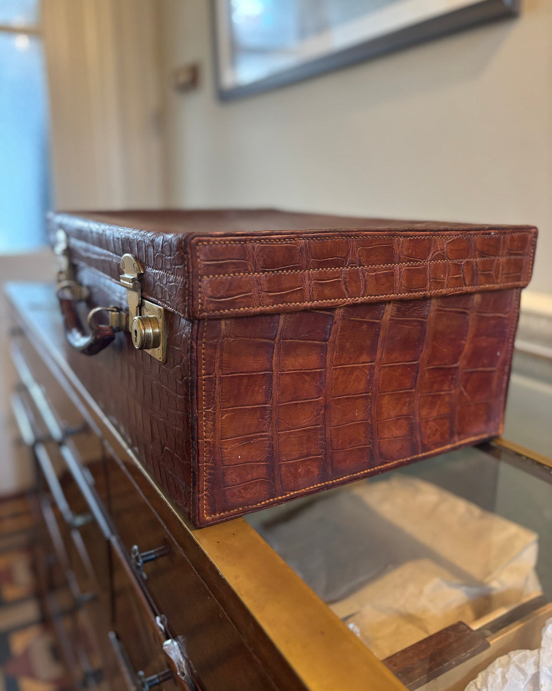 Brown crocodile-patterned suitcase on a glass surface with a blurred background