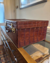 Brown crocodile-patterned suitcase on a glass surface with a blurred background