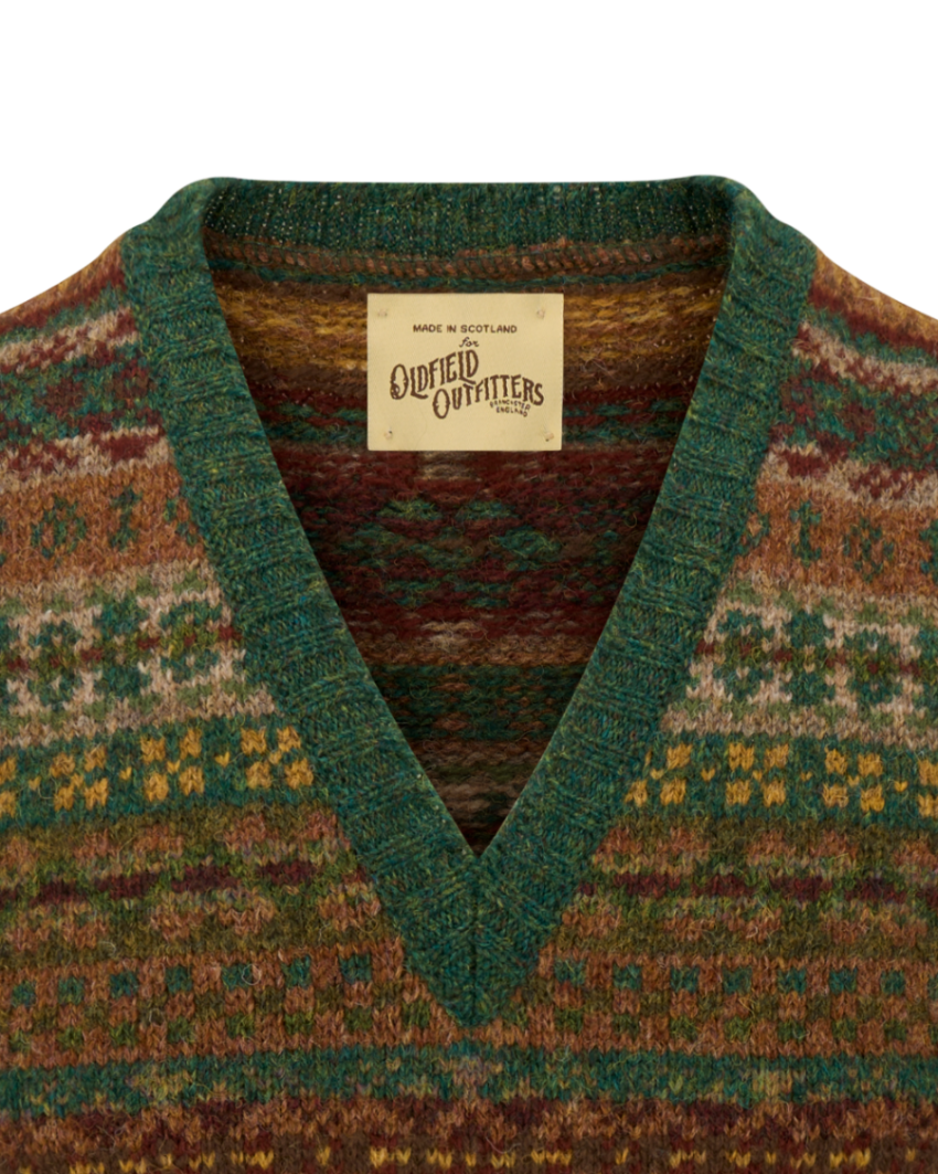 Close-up of a knit V-neck sweater with a green ribbed v-neck collar and a cream woven label reading 'Made in Scotland' and 'Cumniff Outfitters Co.'.