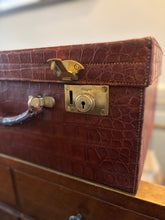 Brown crocodile skin suitcase with gold lock on a wooden surface