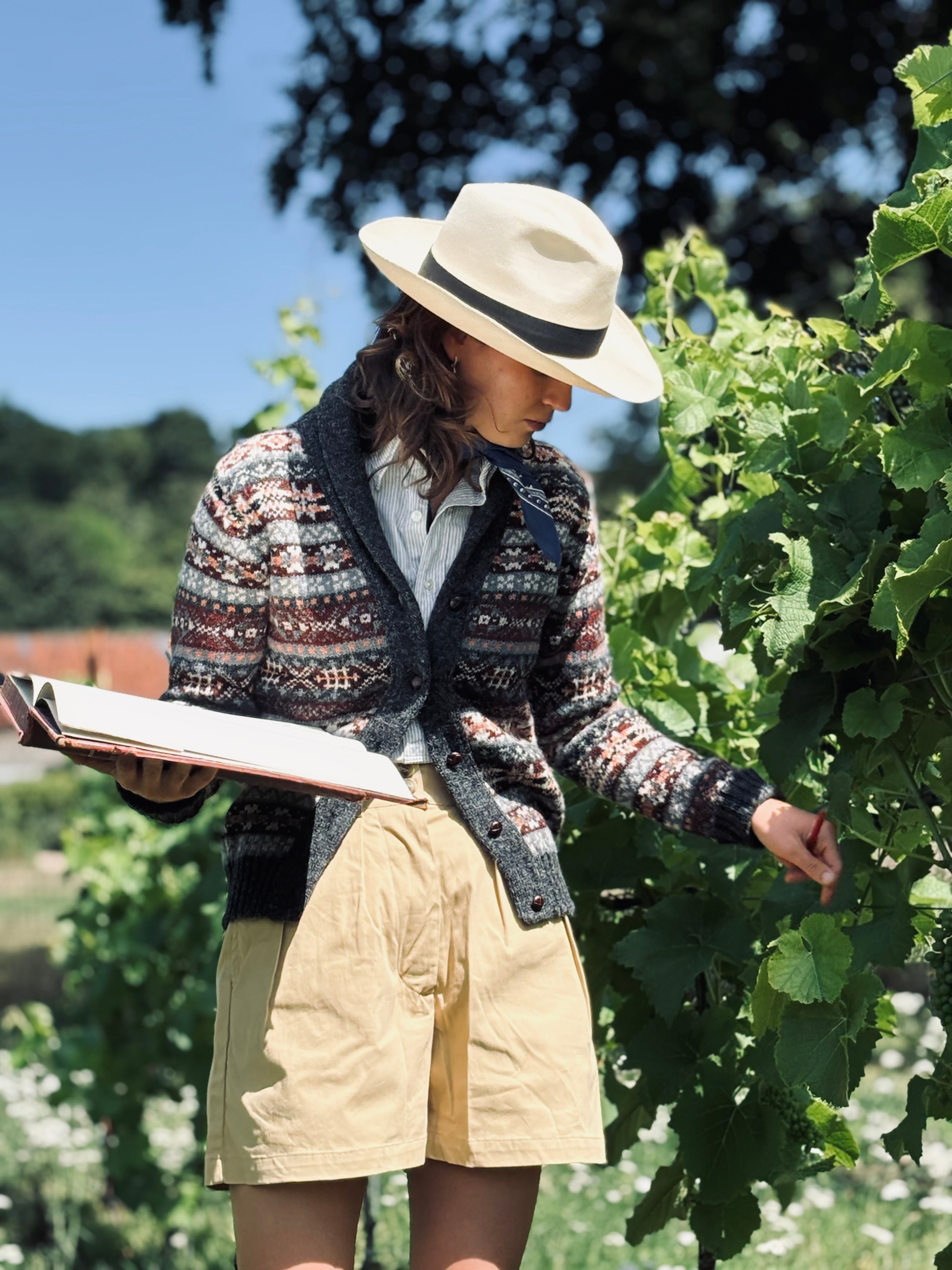 Woman in a patterned Fair Isle cardigan and vintage hat examining something in a garden