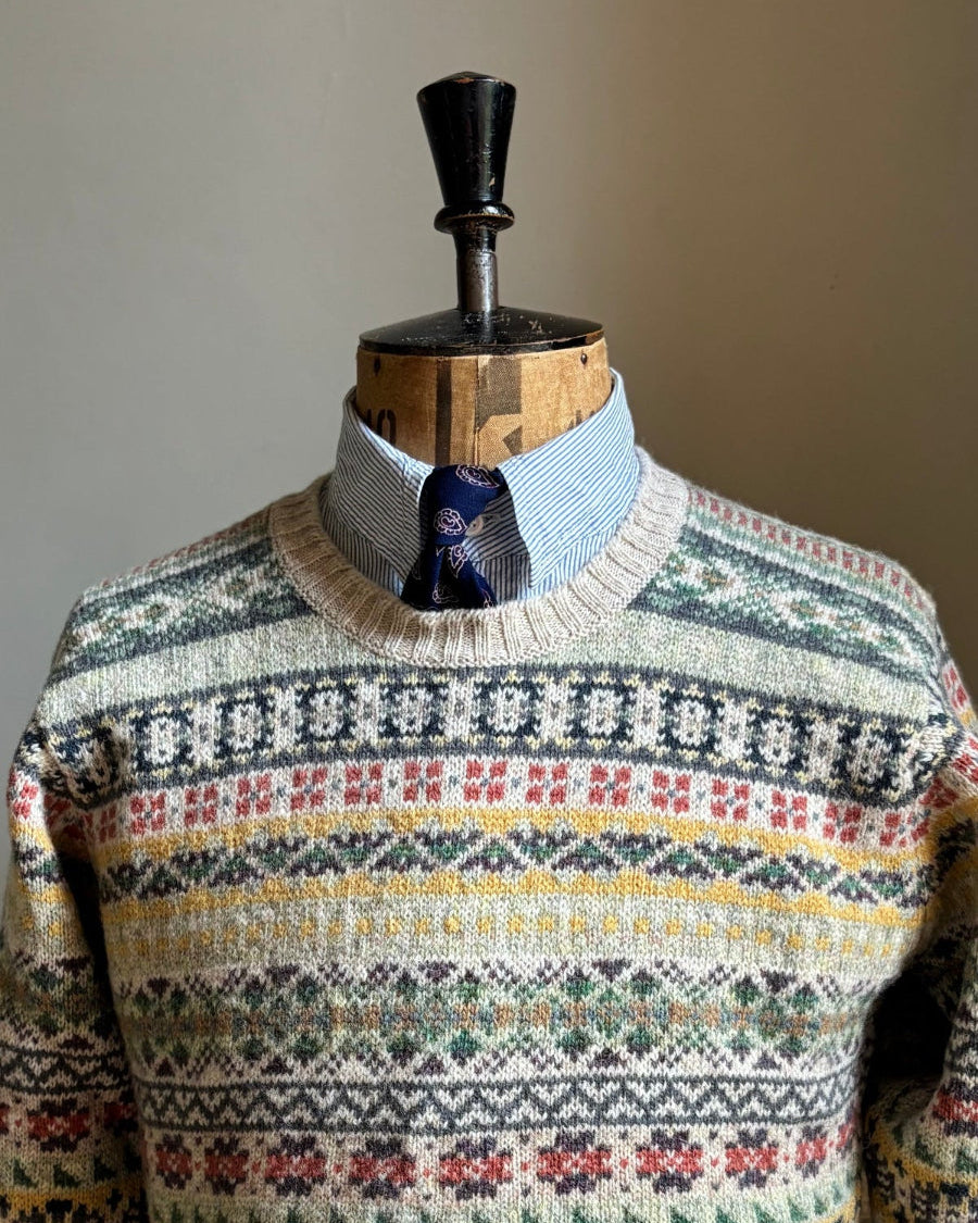 A multicolor Fair Isle knit sweater displayed on a wooden dress form mannequin, styled with a light blue collared shirt and a blue patterned tie underneath.