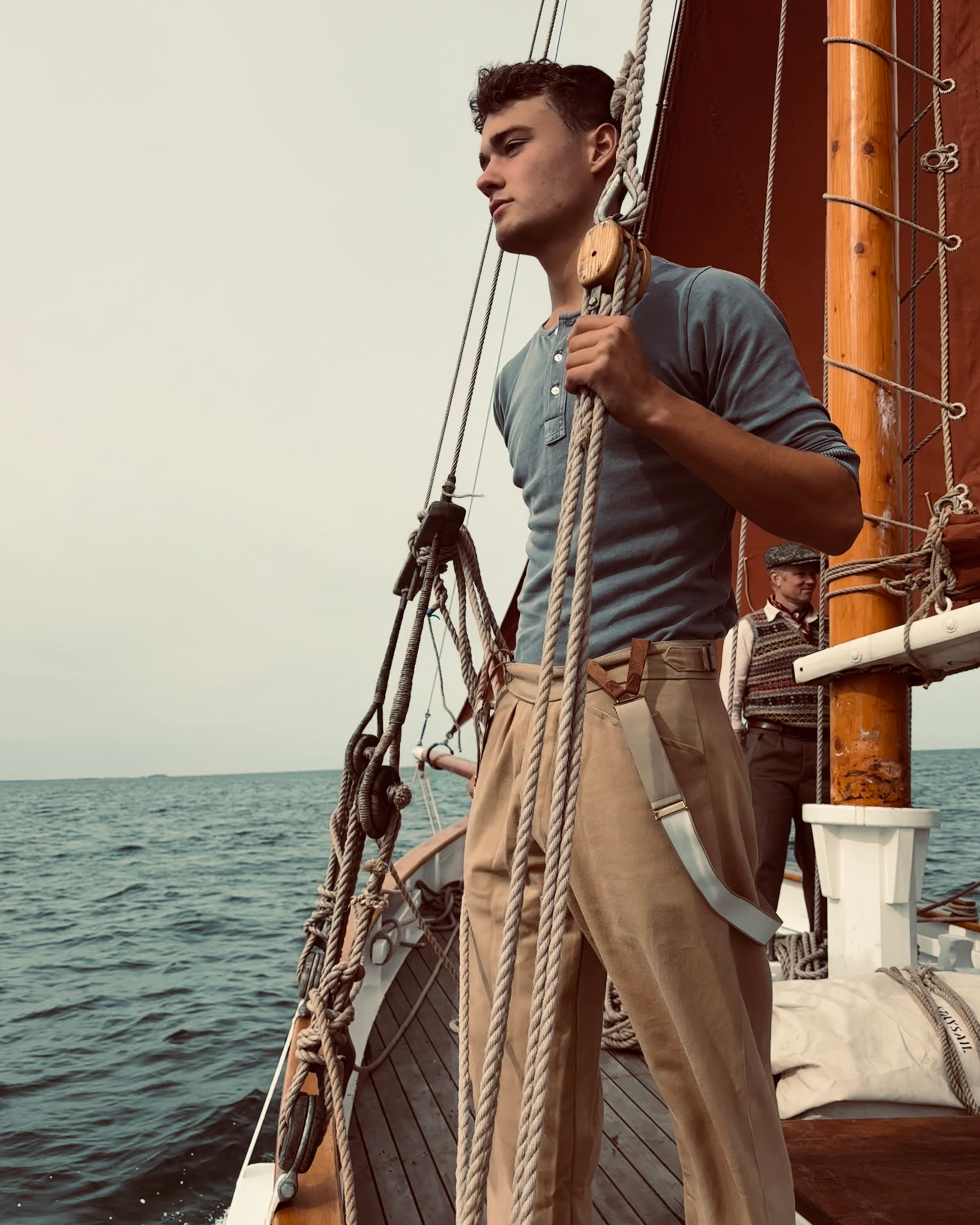 Man on a ship with ropes and wooden structure, sea in the background