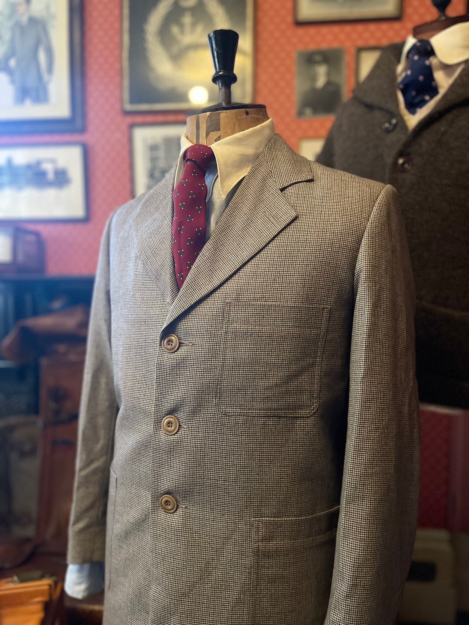 A vintage 1940s style brown dogtooth tweed suit on a mannequin, featuring a jacket with 1940s lapels and corozo buttons, and trousers with double pleats.