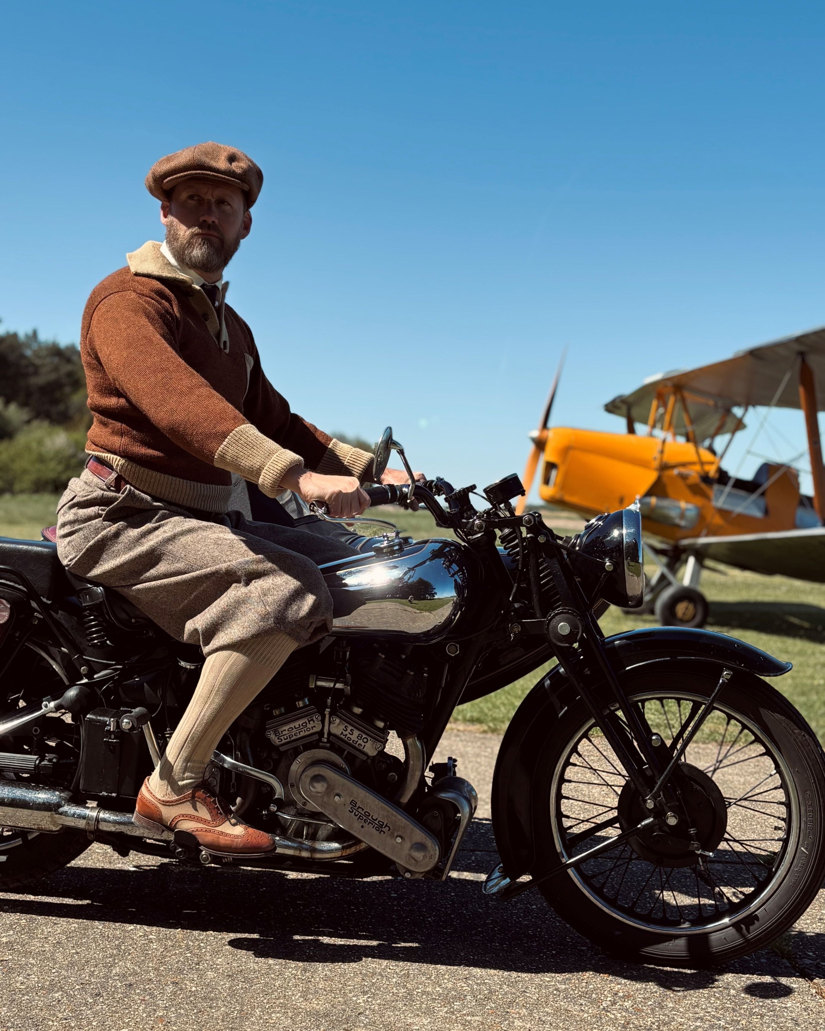 Man riding a vintage motorcycle with a biplane in the background