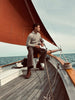Man sitting on a sailboat deck with a red sail and ocean background