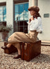 Woman in vintage attire sitting on a suitcase outdoors