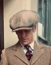 Man wearing a patterned cap and herringbone coat in an urban setting