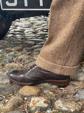 Brown leather shoe on a stone surface with a herringbone patterned leg visible.