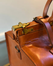 Close-up of a brown leather bag with gold hardware on a neutral background