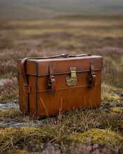 Brown leather suitcase with a gold lock on a grassy field