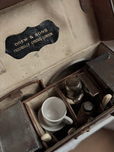 Vintage-style tea set in an open suitcase with 'Drew & Sons' label.