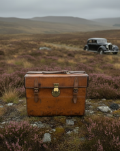 Vintage suitcase in a field with a classic car in the background