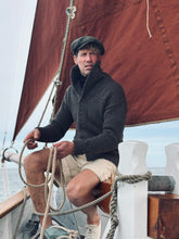Man sitting with heavy knitwear on a vintage wooden sailboat with a red sail