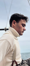 Man wearing a cream turtleneck sweater with a blurred background