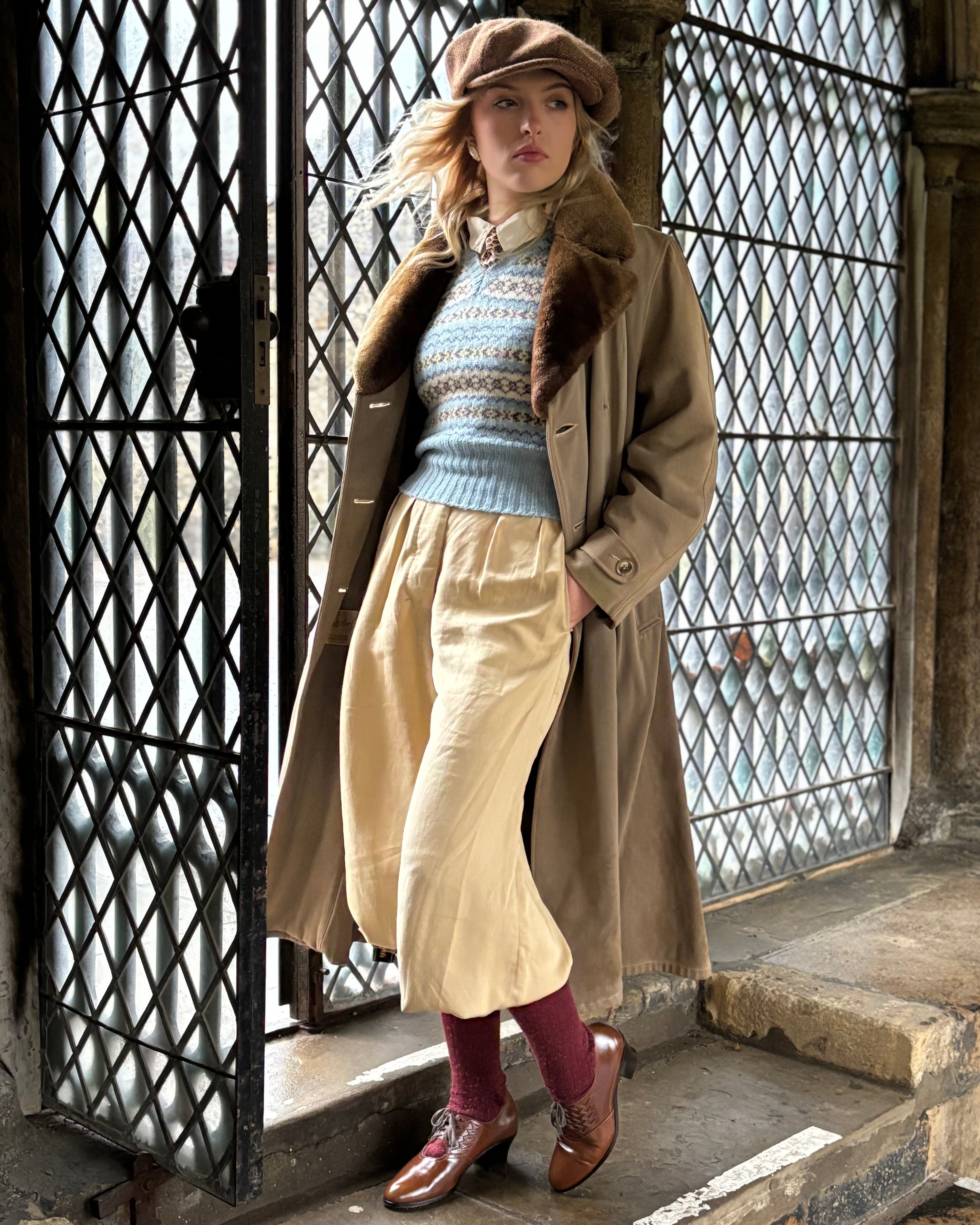 Woman in vintage clothing standing in front of a stone building with lattice windows.