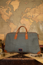 Green travel bag with brown handles on a table with a world map in the background
