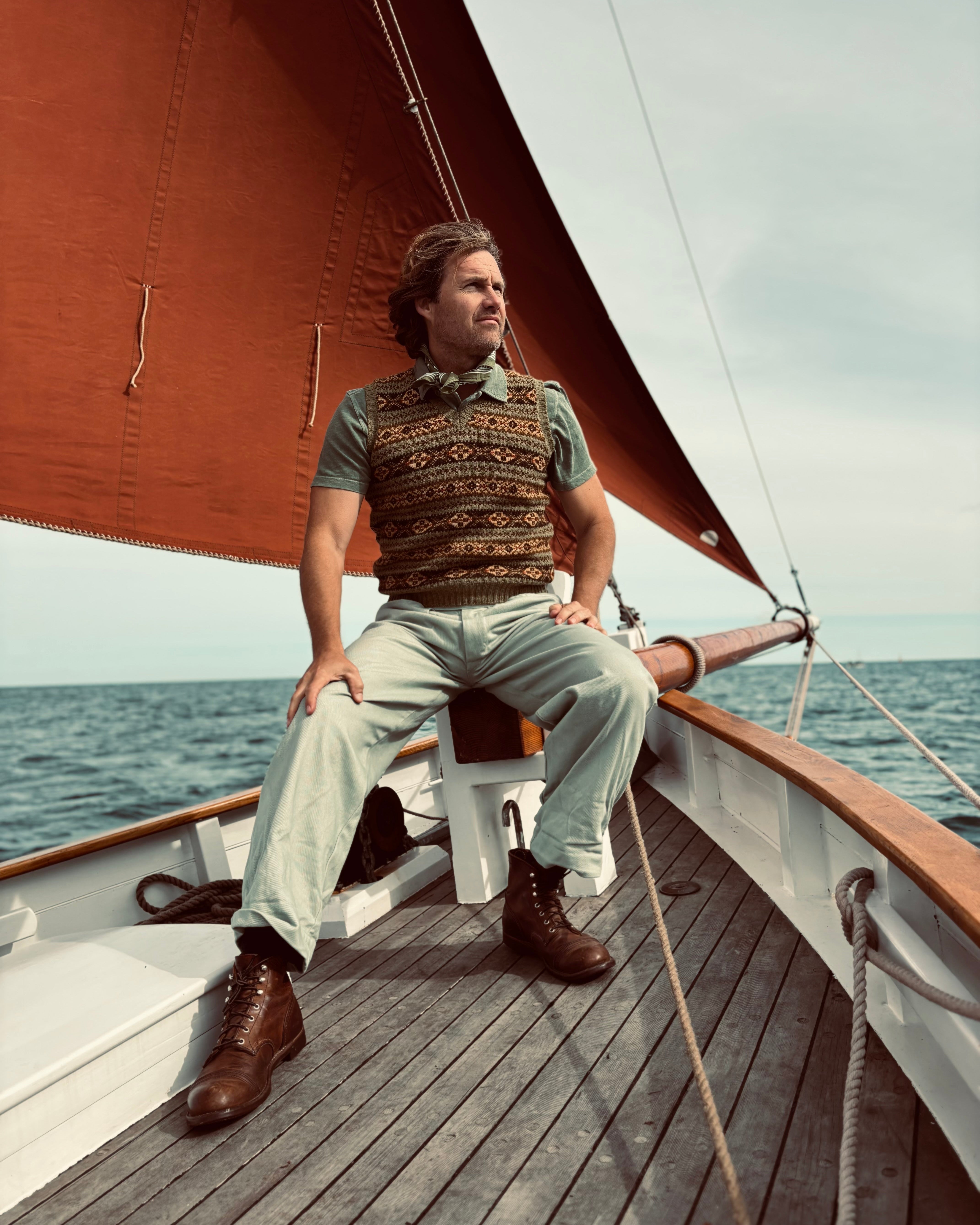 Man sitting on a sailboat deck with a sail in the background