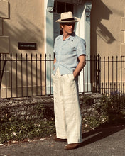 Man wearing a hat and light-colored vintage linen trousers standing in front of a building with a metal gate.